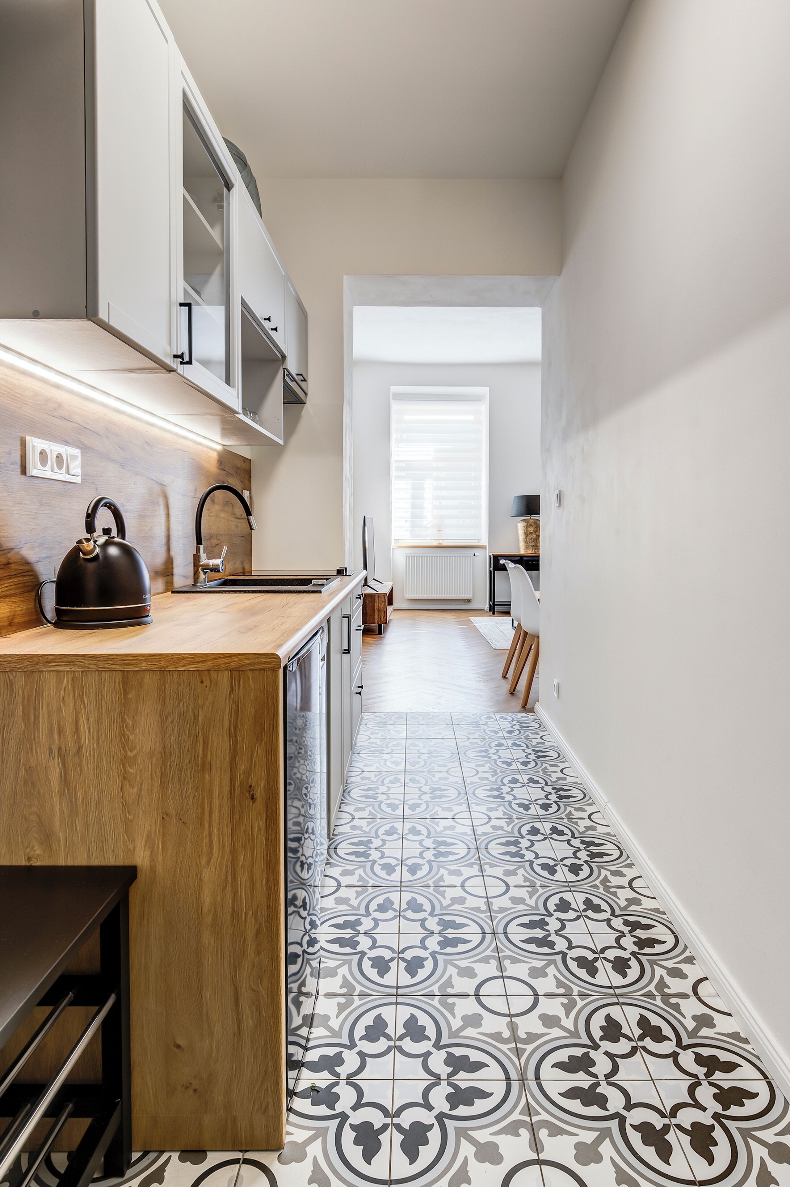 A modern kitchen with a wooden countertop, a kettle, and a patterned tile floor.