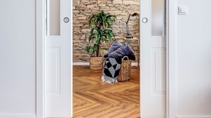 Une pièce dotée d’un parquet en bois disposé en motif à chevrons, d’une porte blanche donnant sur un mur en pierre et d’une plante dans un panier tressé.