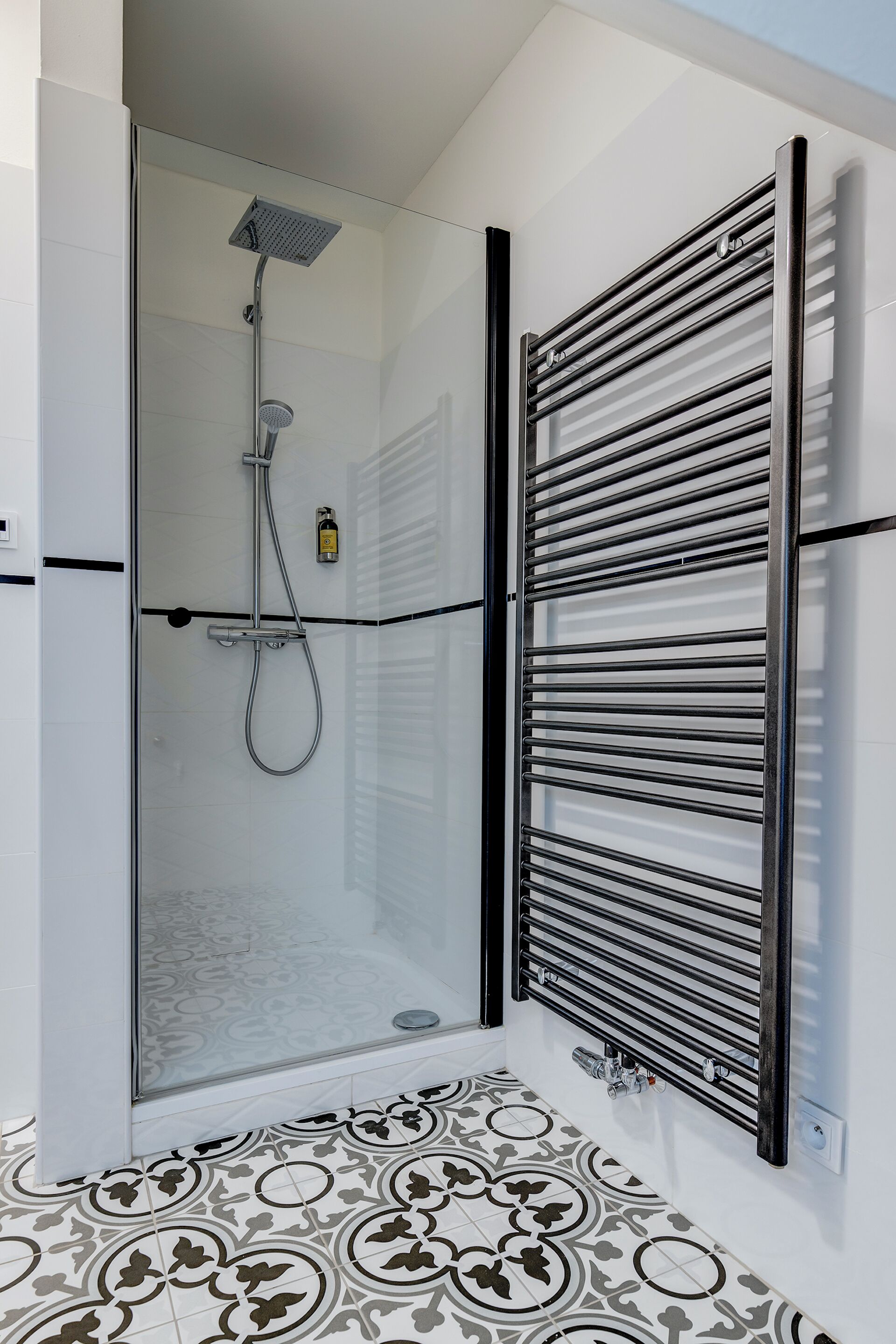 Une salle de bain moderne avec une douche à parois de verre, un porte-serviettes noir et des carreaux de sol à motifs.