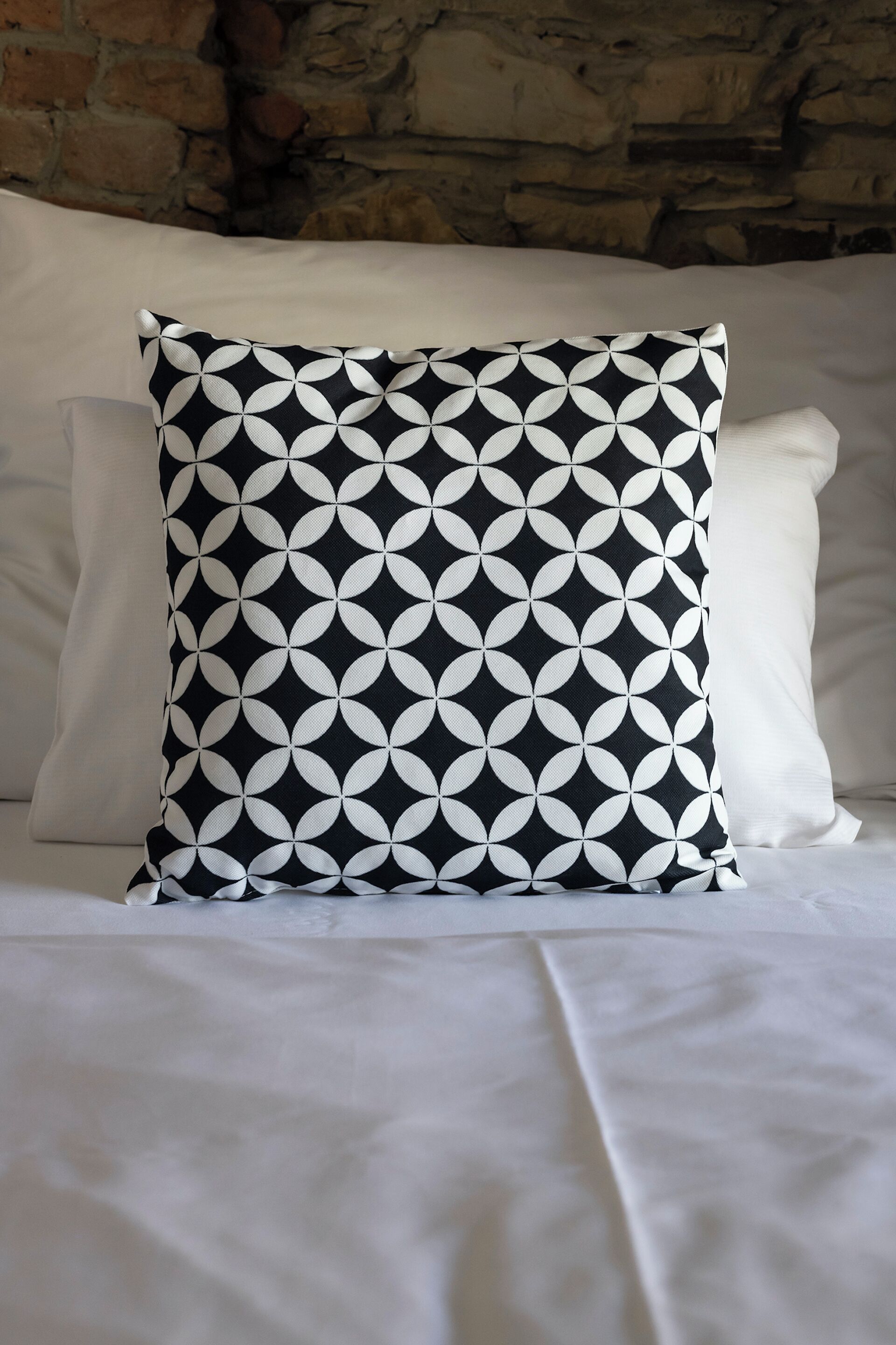 A bed with a black and white patterned pillow, white pillows, and a white bedspread.