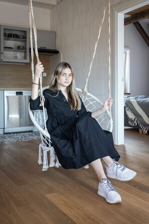 A person sitting on a rope swing chair in a room with a kitchen in the background.