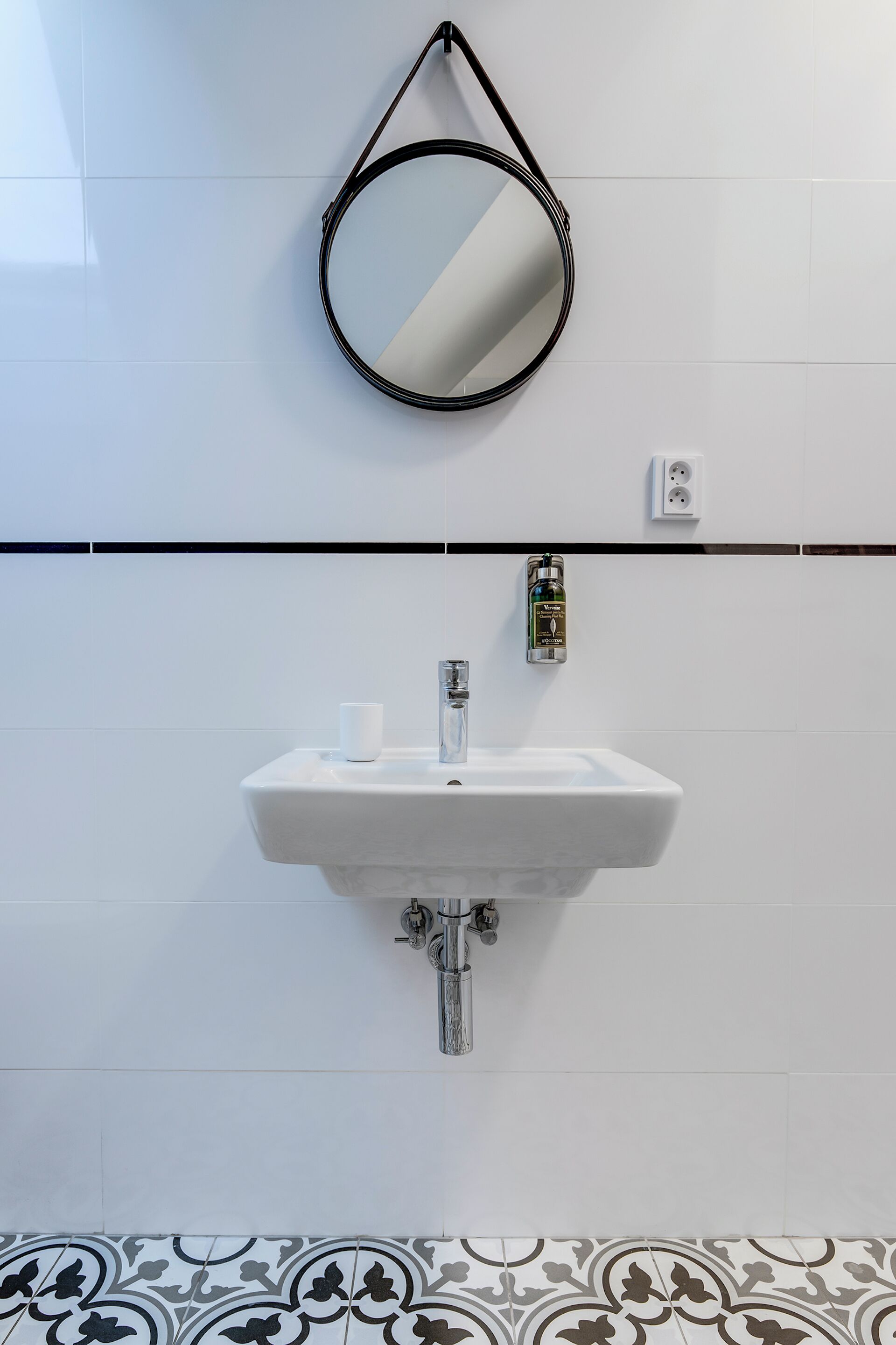 Une salle de bain avec un lavabo blanc, un miroir rond et des carreaux de sol à motifs.