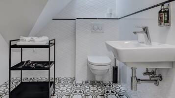 Un baño moderno con repisa metálica negra, lavamanos blanco y baldosas de suelo estampadas.