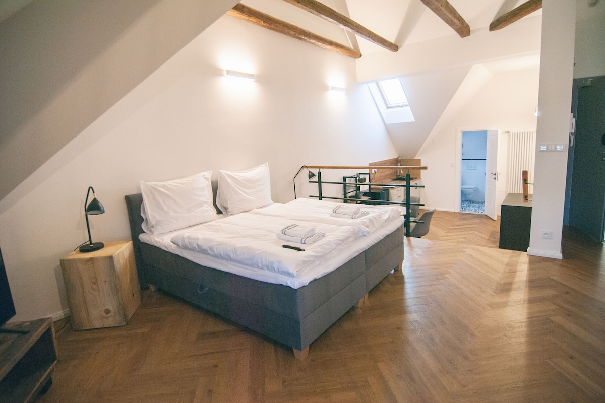 A bedroom with a bed, wooden flooring, a skylight, and a built-in desk with a chair.