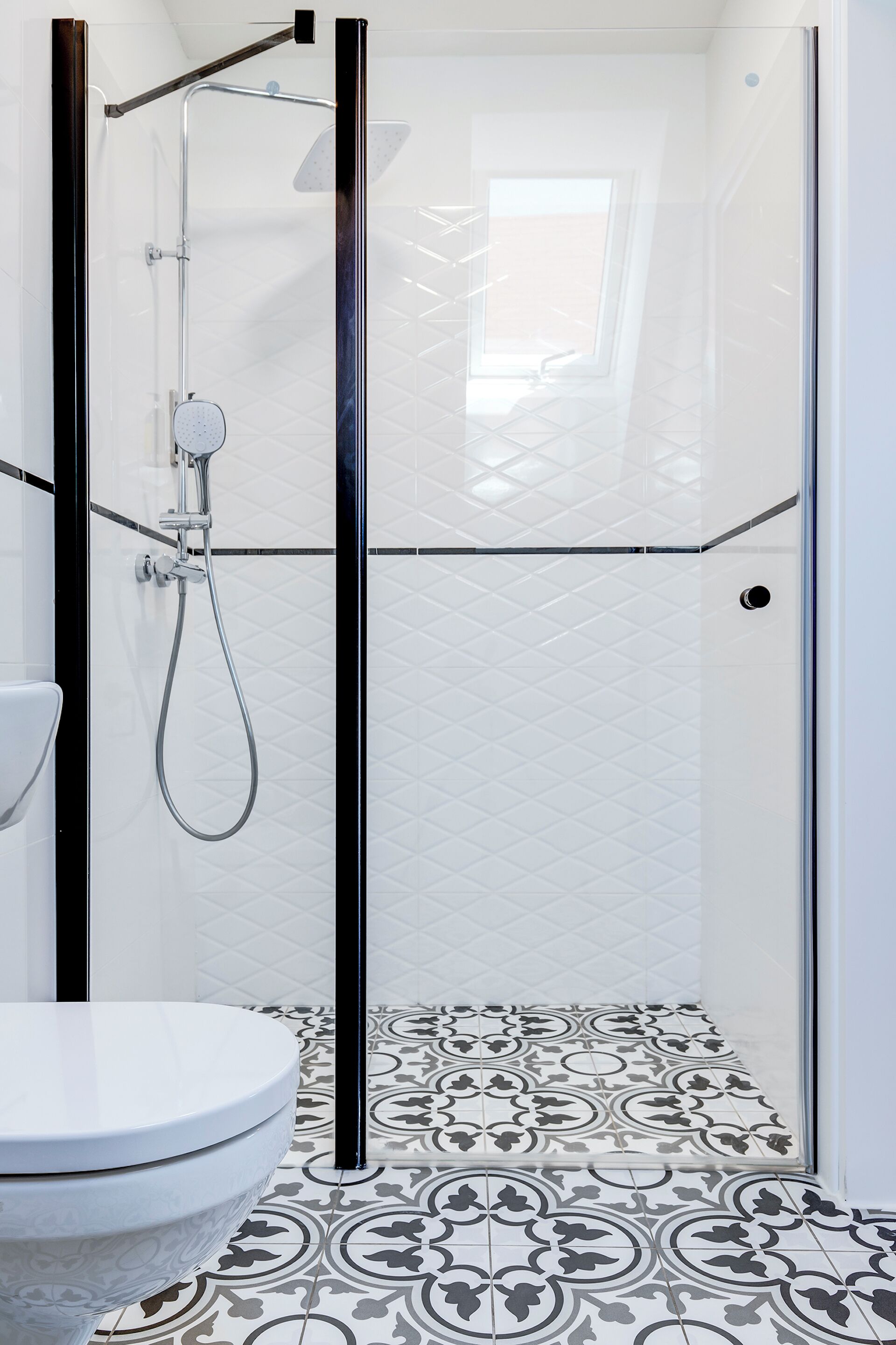 A modern bathroom with a glass-enclosed shower, a white toilet, and patterned floor tiles.