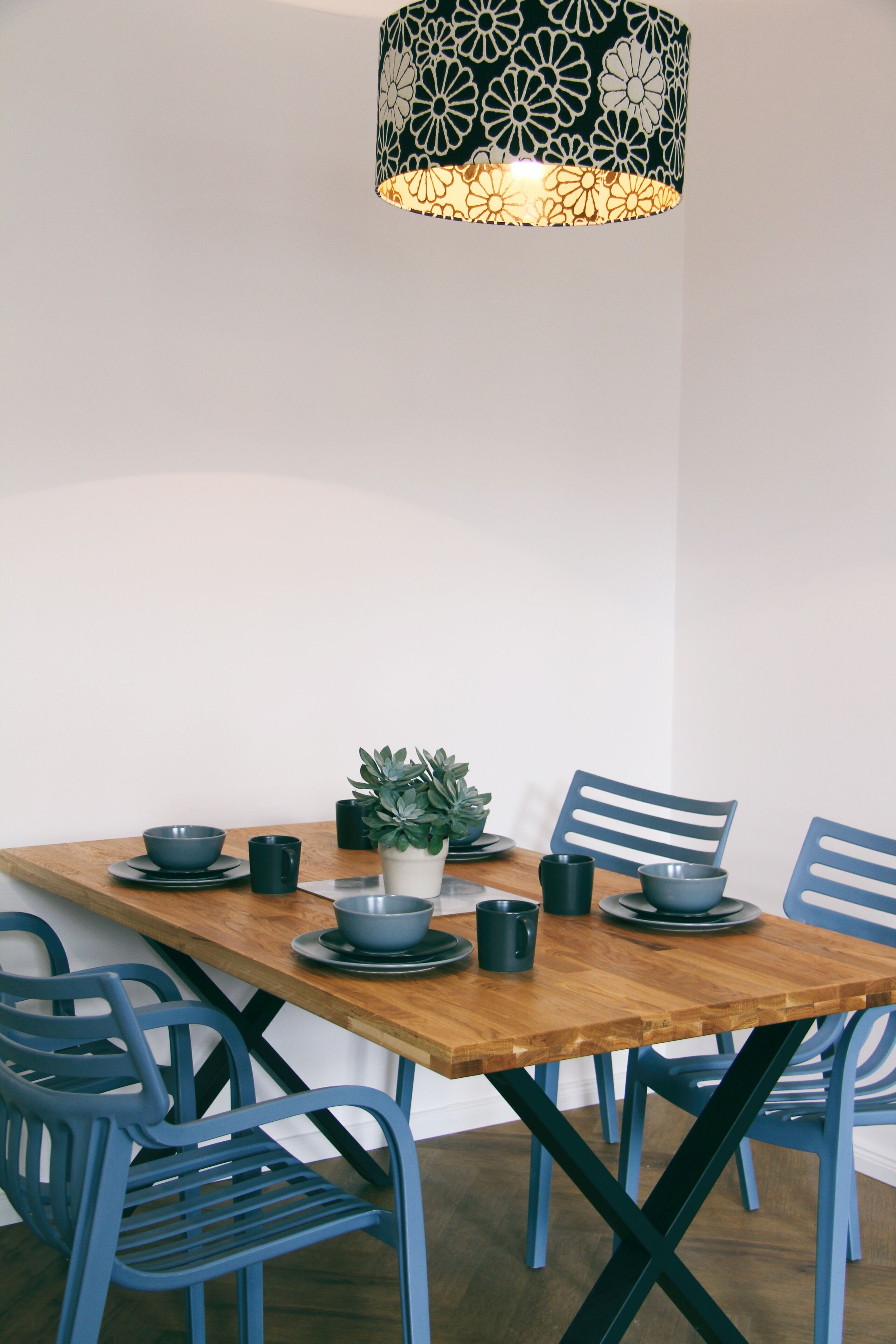 Une table à manger avec des chaises bleues, une plante en pot et une suspension aux motifs noir et blanc.