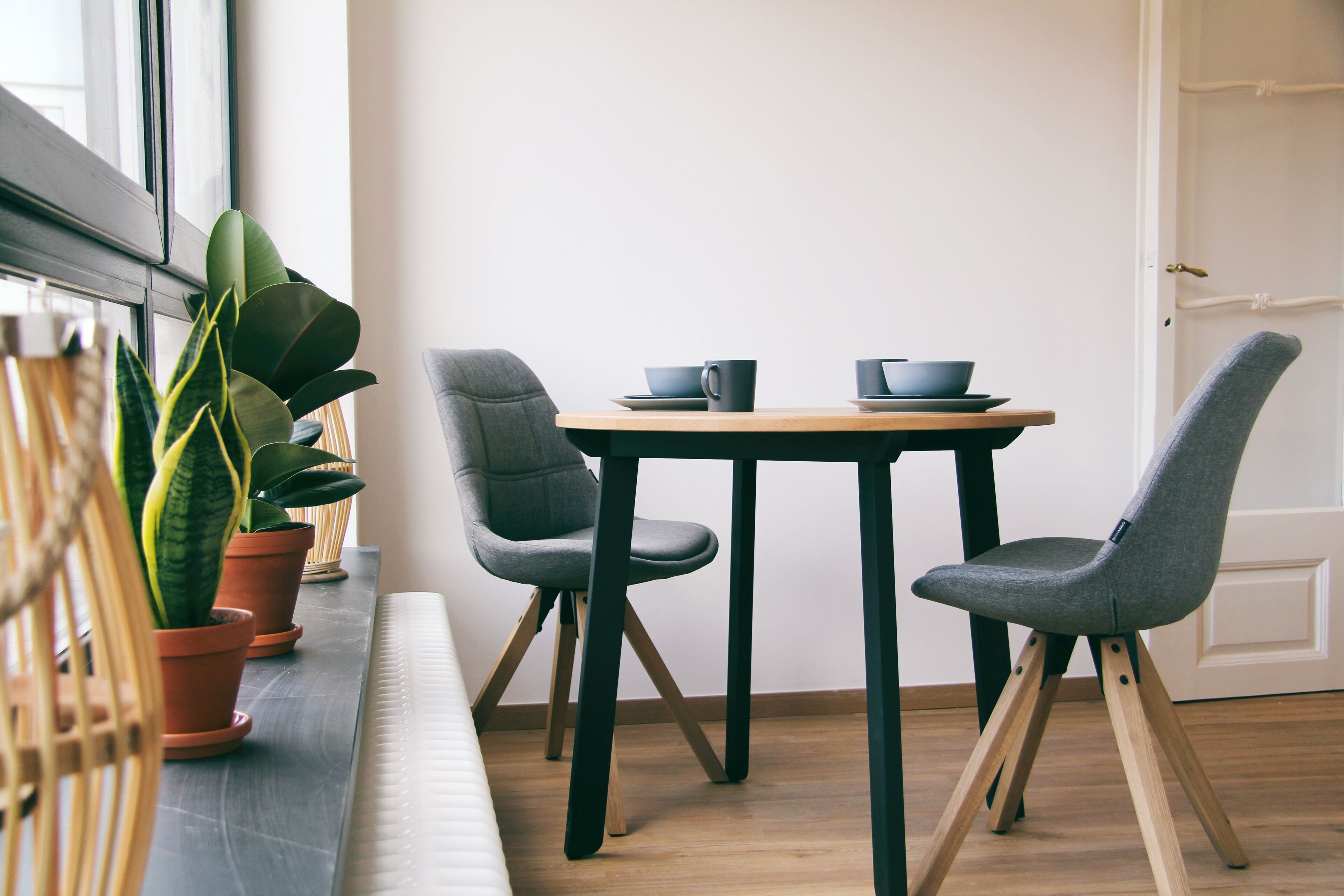 Uma área de refeições moderna com uma mesa redonda, duas cadeiras cinzentas e plantas em vasos.