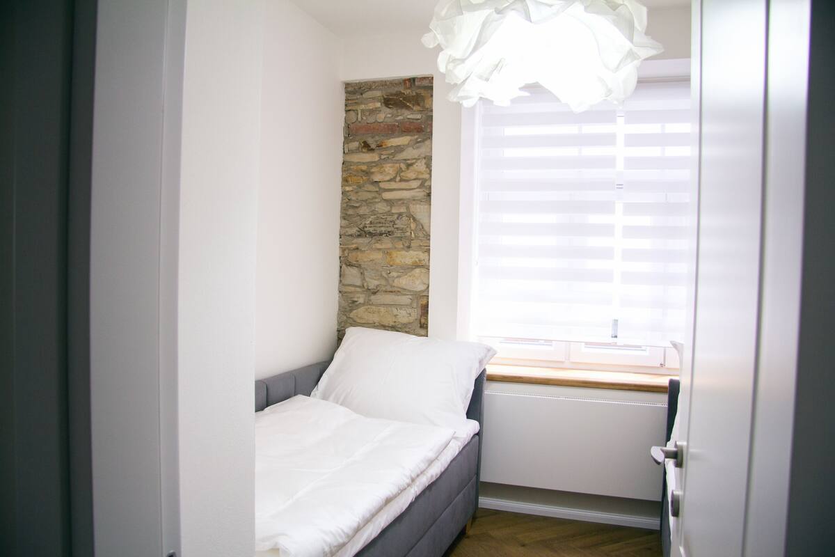 A small bedroom with a bed, a stone wall, a window with blinds, and a radiator.