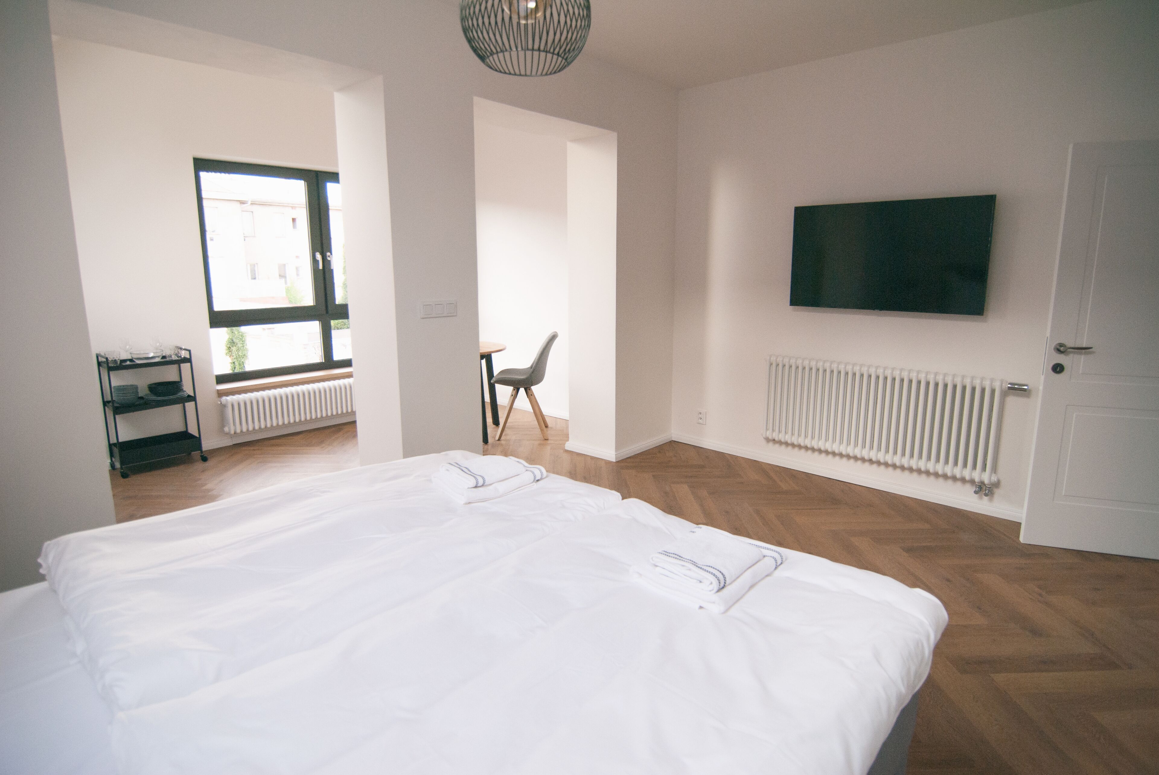 A modern hotel room with a large bed, a TV mounted on the wall, and a window providing natural light.