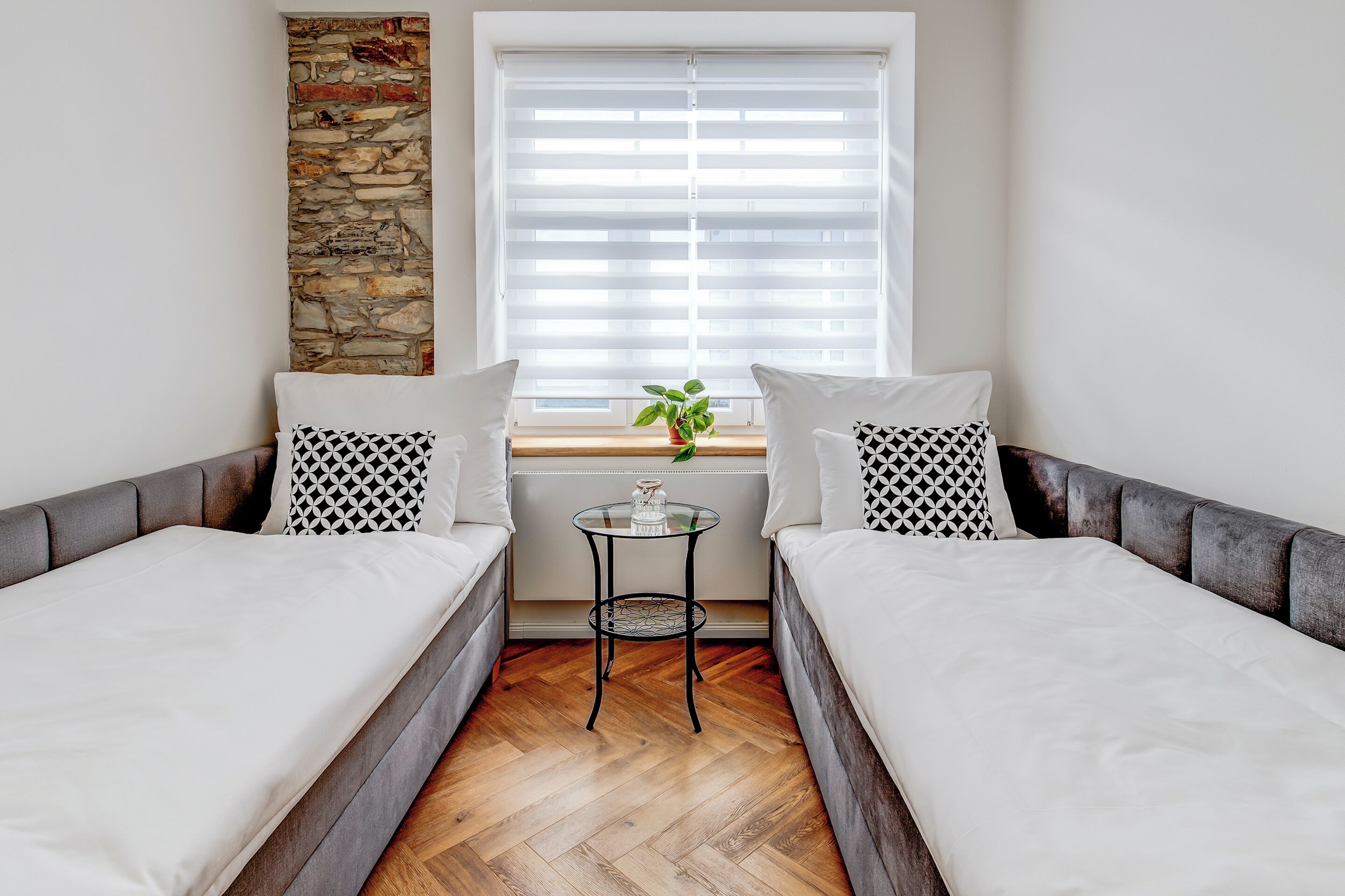 A modern room with two beds, a small table, and a window with blinds.