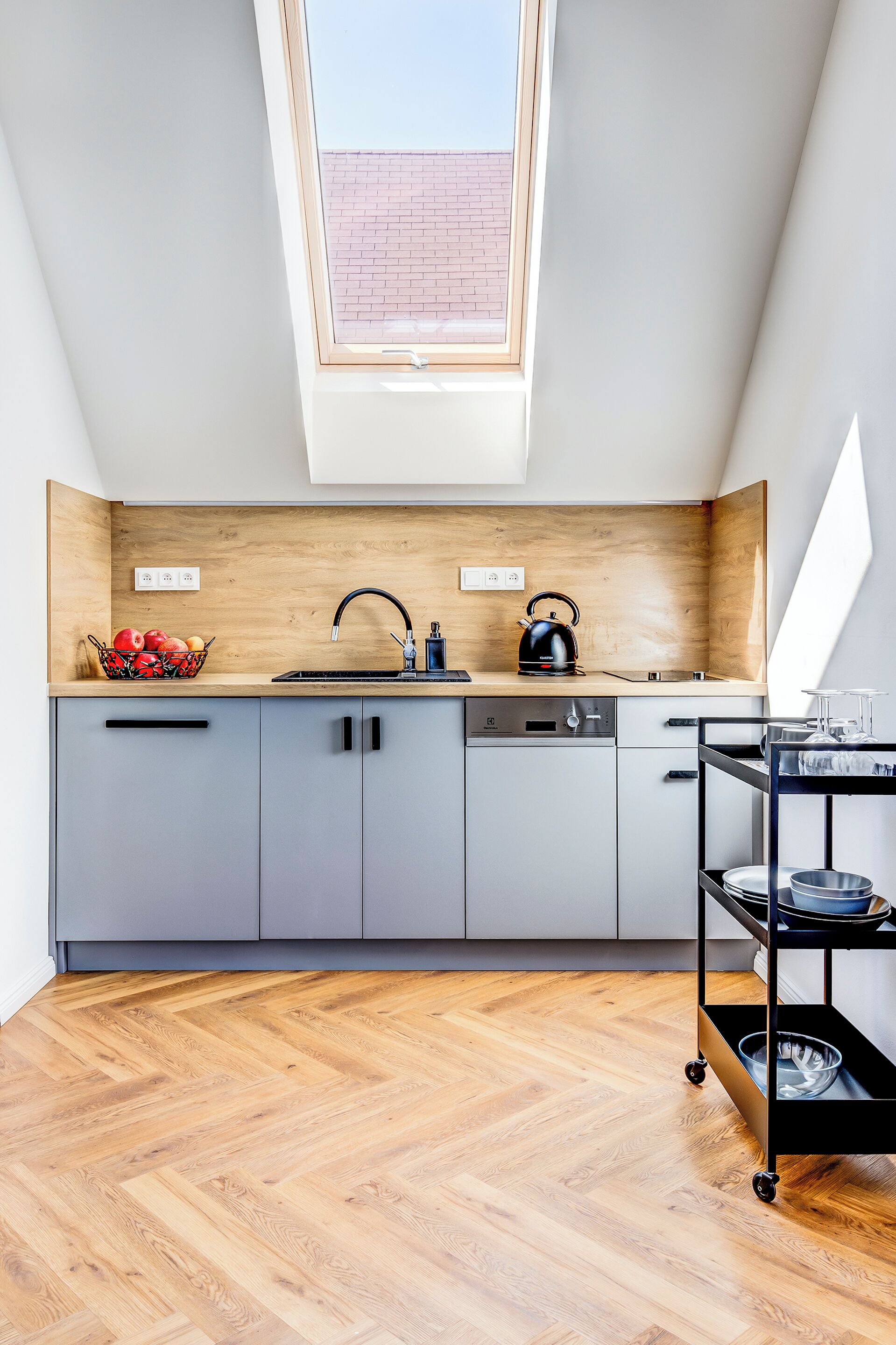 A modern kitchen with a skylight, grey cabinets, a wooden countertop, and a black kettle.