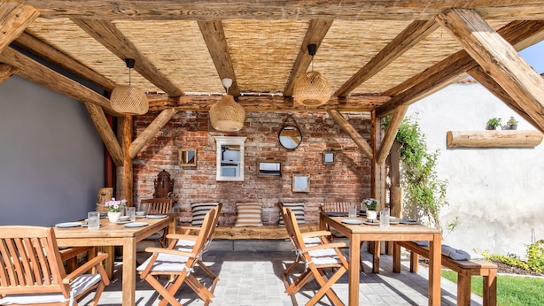Un espace de restauration en plein air avec des tables et des chaises en bois, un mur en briques et un toit de chaume.