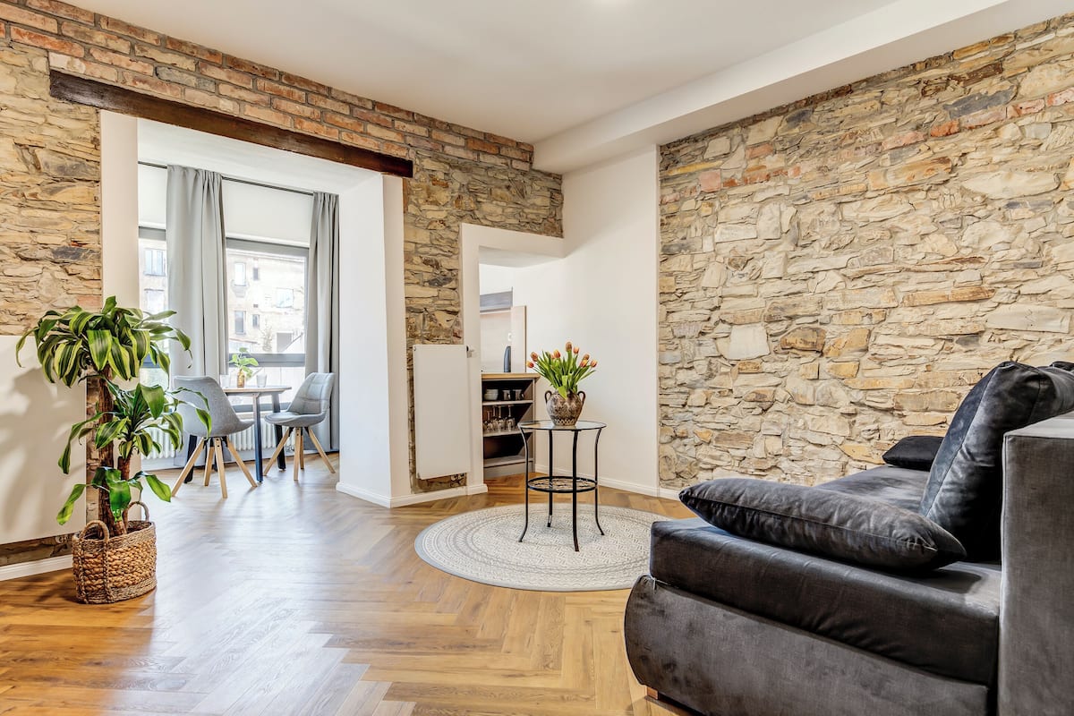 A modern living room with a stone wall, wooden flooring, a grey sofa, and a small round table with a plant.