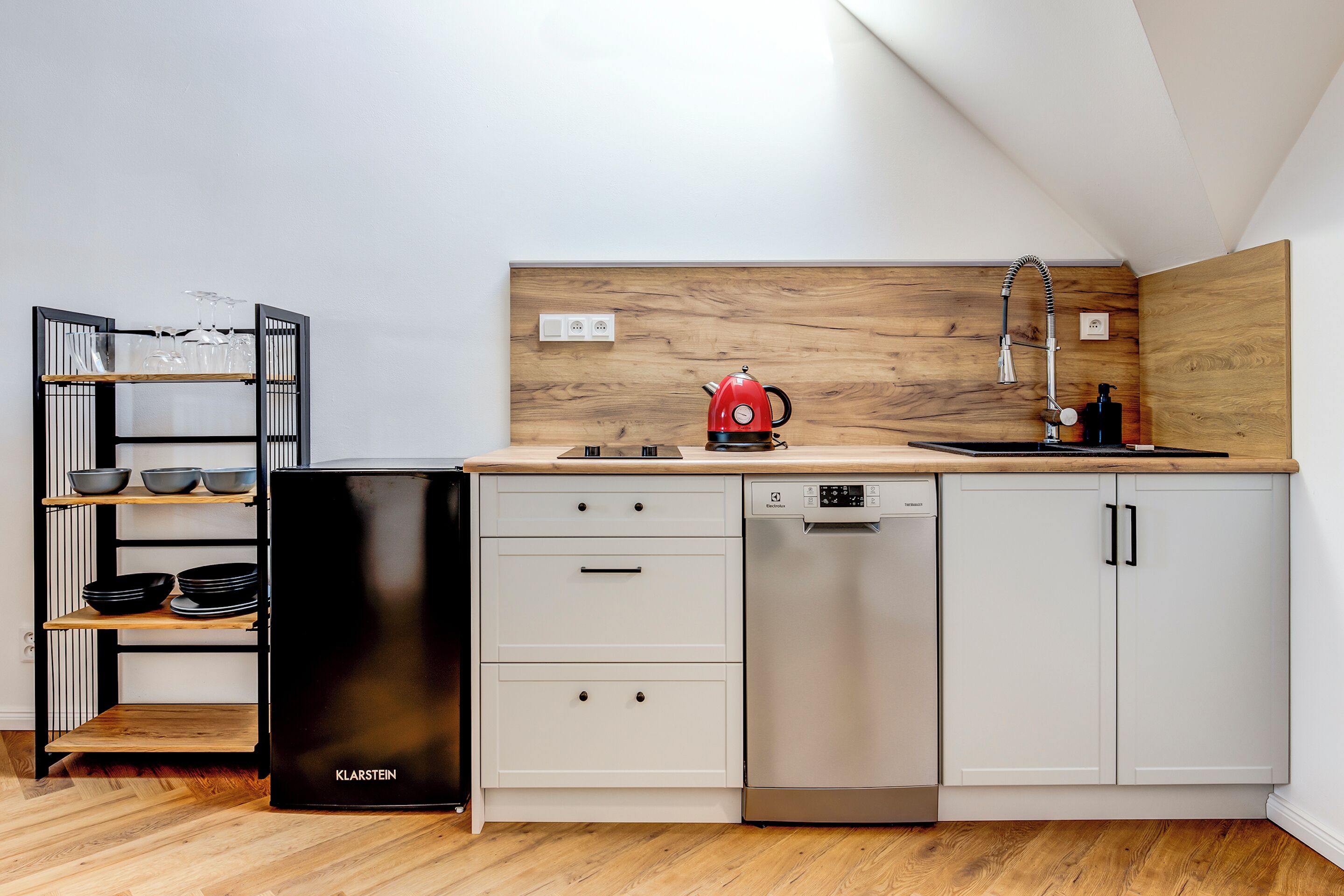 Una cocina moderna con un refrigerador negro, armarios blancos, encimera de madera, un hervidor rojo y un lavavajillas.