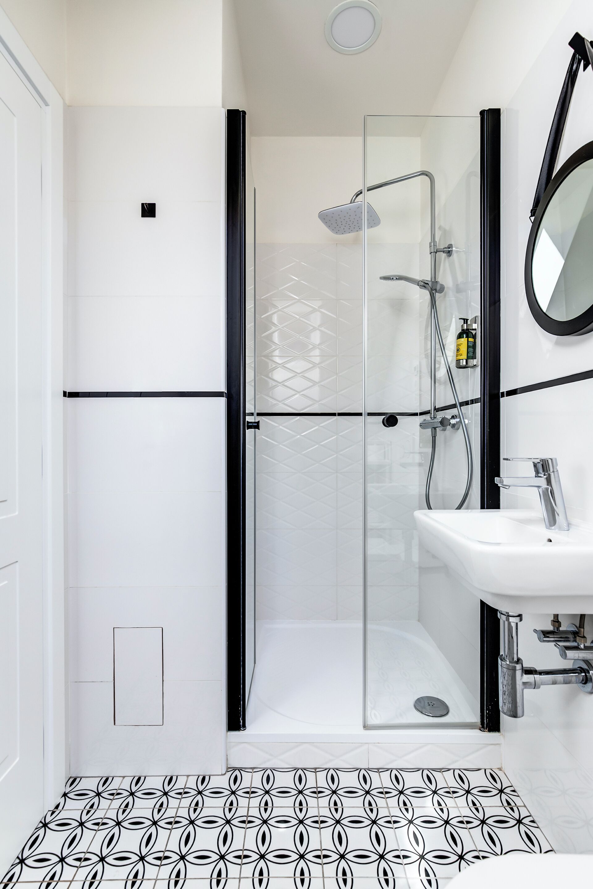 Un baño moderno con ducha de vidrio, lavamanos blanco y piso estampado.