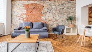 Un salon avec un mur en pierre, un canapé gris, une table basse en bois et une table à manger blanche.