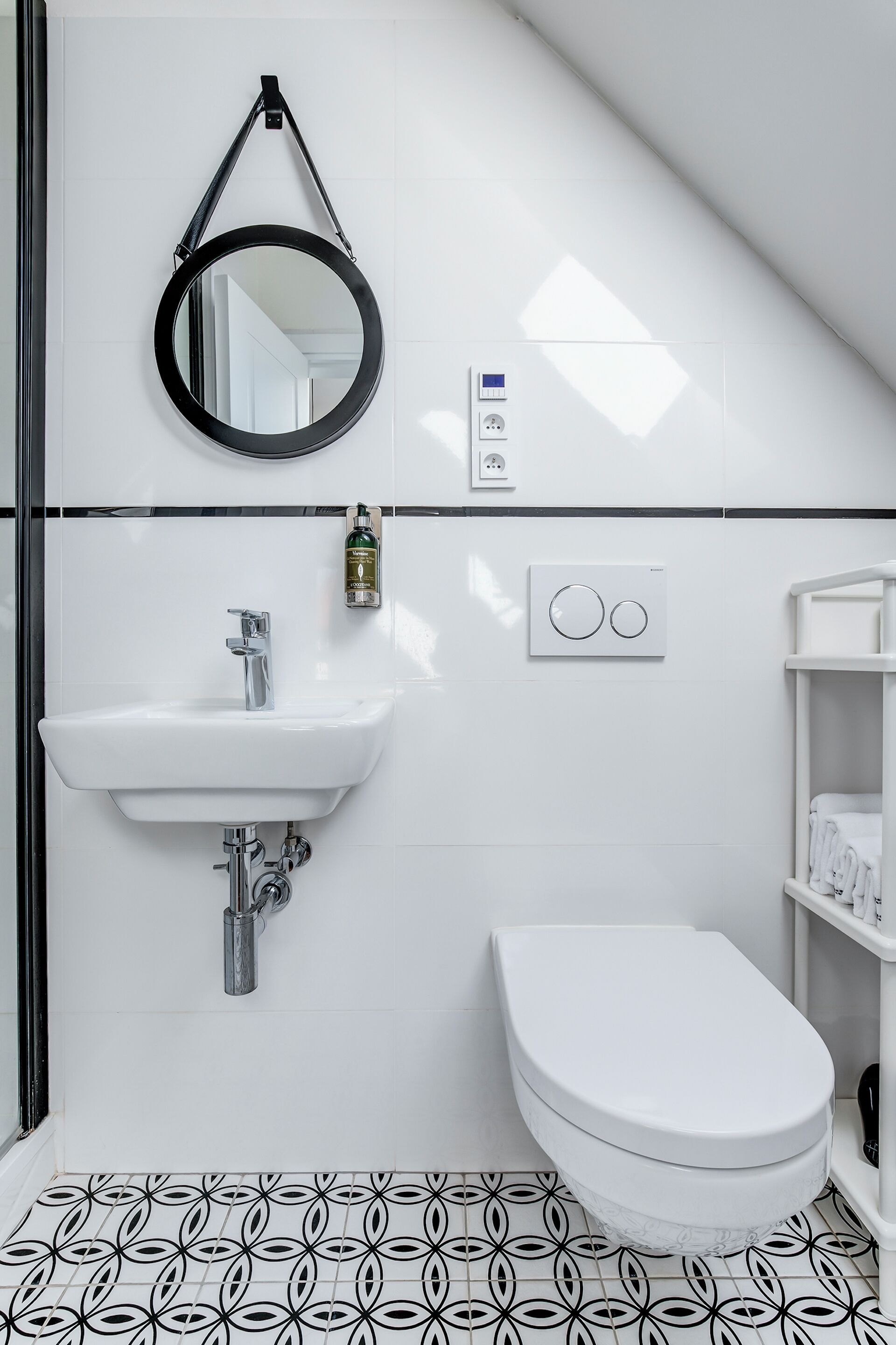 A modern bathroom with a white sink, toilet, and a black circular mirror.