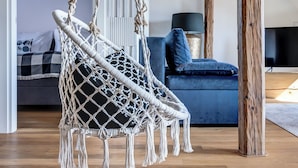 Un fauteuil suspendu dans une pièce avec des poutres en bois, un canapé bleu et un téléviseur.