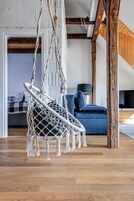 Uma cadeira rede em um quarto com vigas de madeira, um sofá azul e uma televisão.