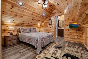 A wooden-paneled bedroom with a bed, nightstand, lamp, and a television on the wall. - Beside Still Water 1 - 2 Bedrooms, 2 Baths, Sleeps 6 Home by RedAwning (Cosby)