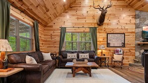 A cozy log cabin interior with a brown leather sofa, a wooden coffee table, and a mounted deer head. - Beside Still Water 1 - 2 Bedrooms, 2 Baths, Sleeps 6 Home by RedAwning (Cosby)