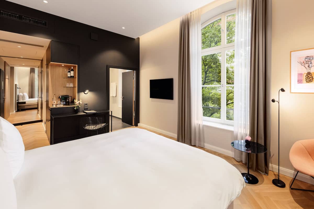 Ein modernes Hotelzimmer mit einem großen Bett, einem Schreibtisch mit Stuhl, einem Fernseher und einem Fenster mit Vorhängen.
