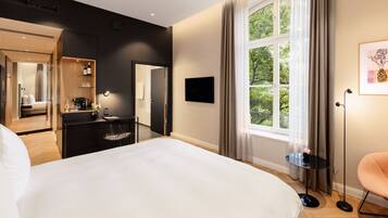 A modern hotel room with a large bed, a desk with a chair, a television, and a window with curtains.