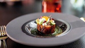 A plated dish with a seared steak, garnished with vegetables and sauce, on a dark plate. - ESPLANADE Saarbrücken (Saarbrücken)