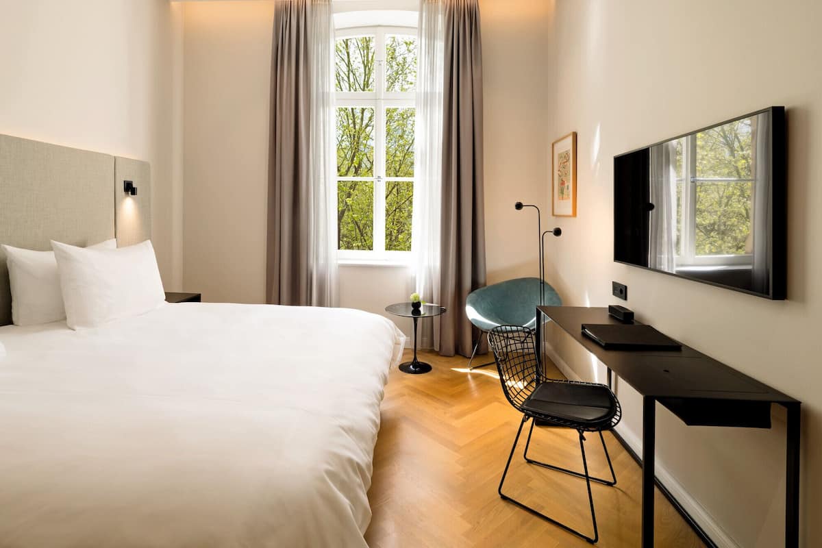 Ein modernes Hotelzimmer mit einem großen Bett, einem Schreibtisch mit Stuhl, einem Fernseher und einem Fenster mit Vorhängen.