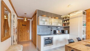 A modern kitchen with a built-in oven, a dining area with a wooden table, and a hallway with wooden doors. - Apartment Amilu - beautiful 7/9 person ski-in, ski-out (Montgenèvre)