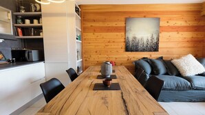 A modern kitchen with white cabinets, a wooden dining table, and a grey sofa with black cushions. - Apartment Amilu - beautiful 7/9 person ski-in, ski-out (Montgenèvre)