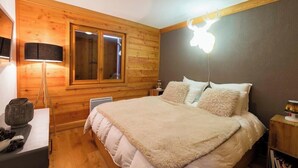 A bedroom with a wooden paneled wall, a large bed with a fluffy blanket, a bedside lamp, and a wall-mounted light fixture. - Apartment Amilu - beautiful 7/9 person ski-in, ski-out (Montgenèvre)