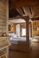 Una cama con dosel de madera en una habitación rústica con pared de piedra y una ventana con cortinas.