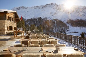 Una terraza de madera con mesas y sillas, con vista a un paisaje montañoso nevado.