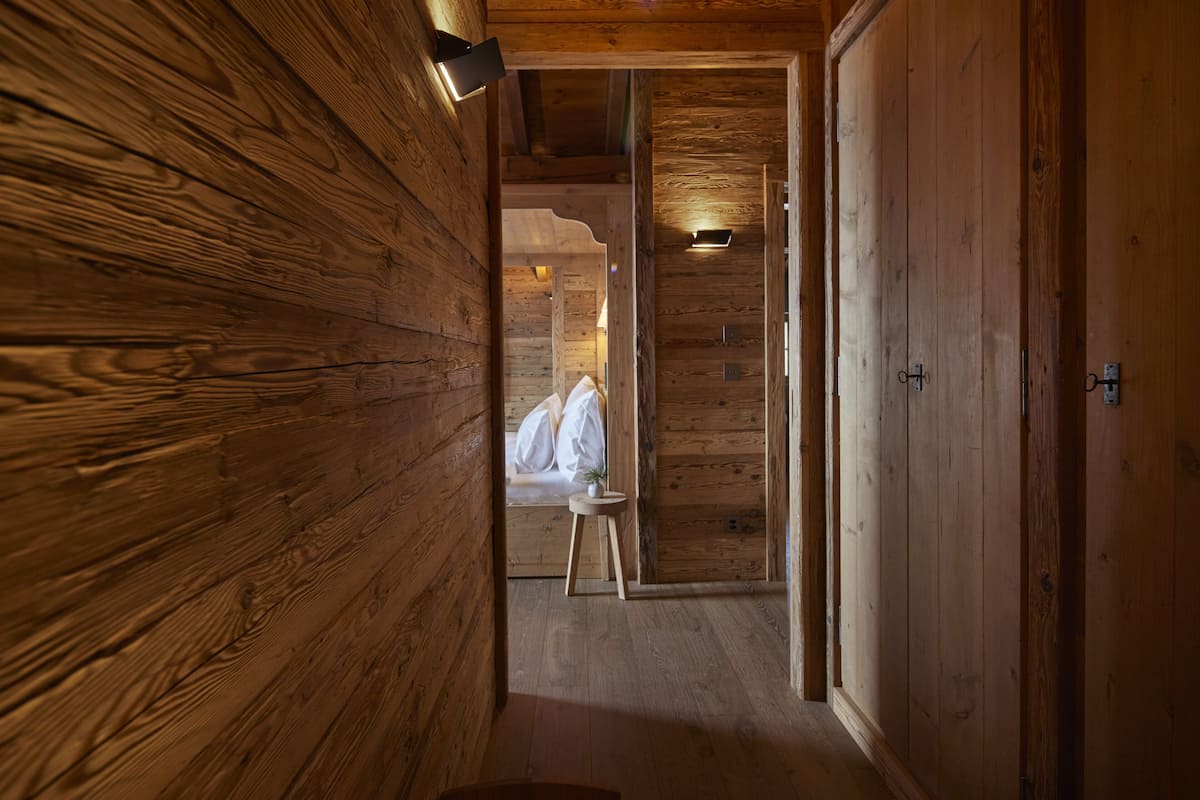 A wooden interior hallway with a bed and a small table.