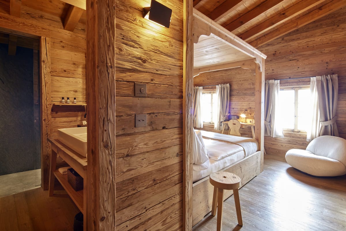 A wooden cabin interior with a bed, a small table, and a chair.