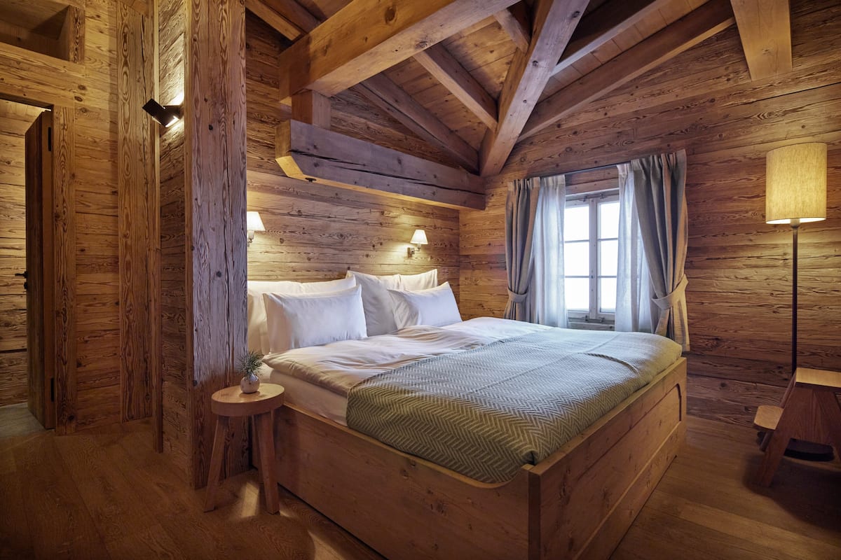 A wooden cabin bedroom with a bed, bedside lamps, and a window with curtains.