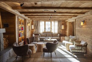 Un acogedor interior de cabaña de madera con un sofá, sillones, una mesita de centro y una estantería.