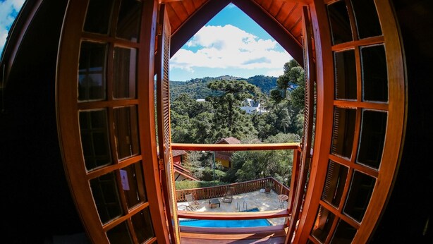 Vista desde un balcón de madera con piscina, que da a una ladera boscosa con casas.