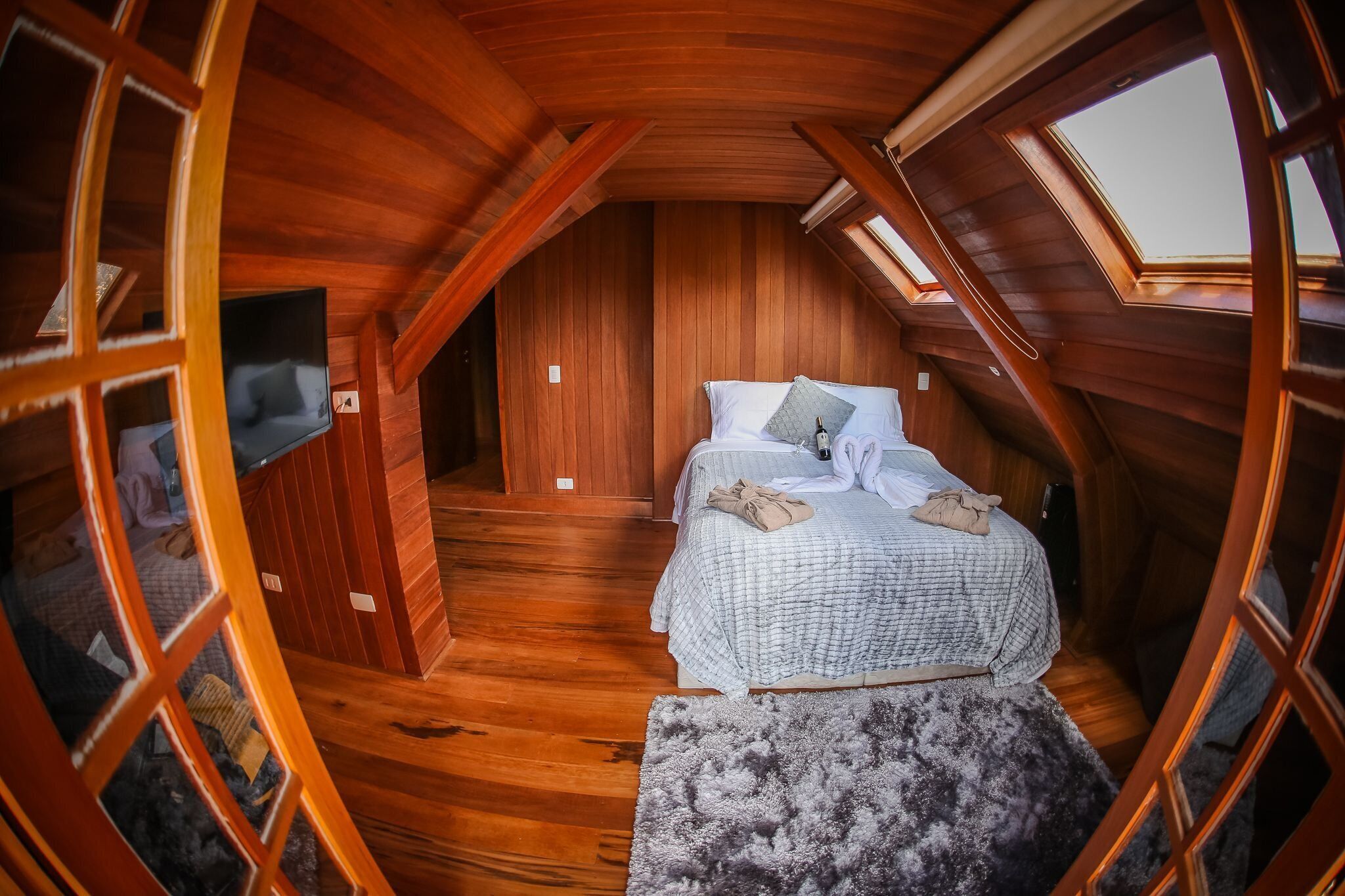 Une chambre confortable située dans les combles, avec des murs en bois, un lit recouvert d’une courtepointe à carreaux et une lucarne.