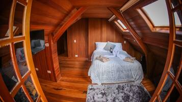 Une chambre confortable située dans les combles, avec des murs en bois, un lit recouvert d’une courtepointe à carreaux et une lucarne.