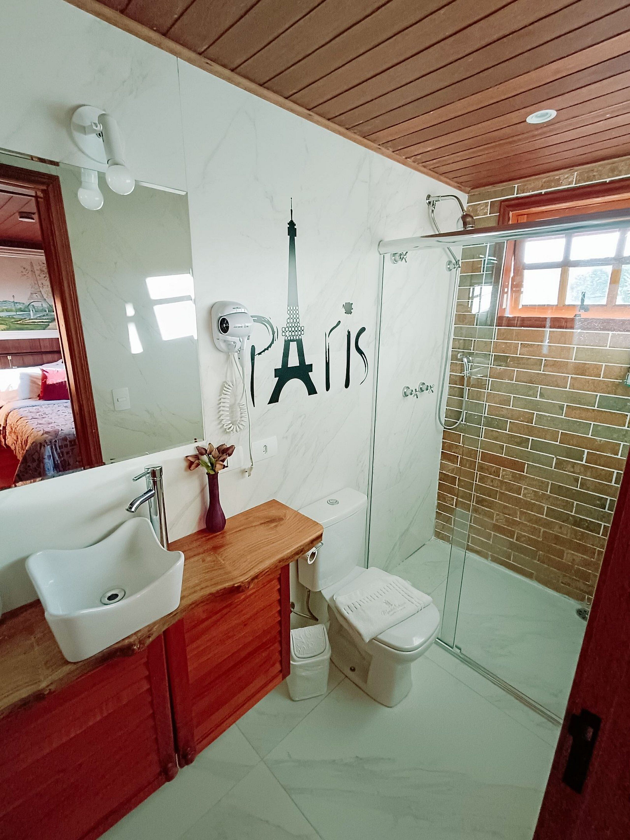 A bathroom with a marble wall, a wooden vanity, a white sink, a toilet, and a glass shower enclosure.