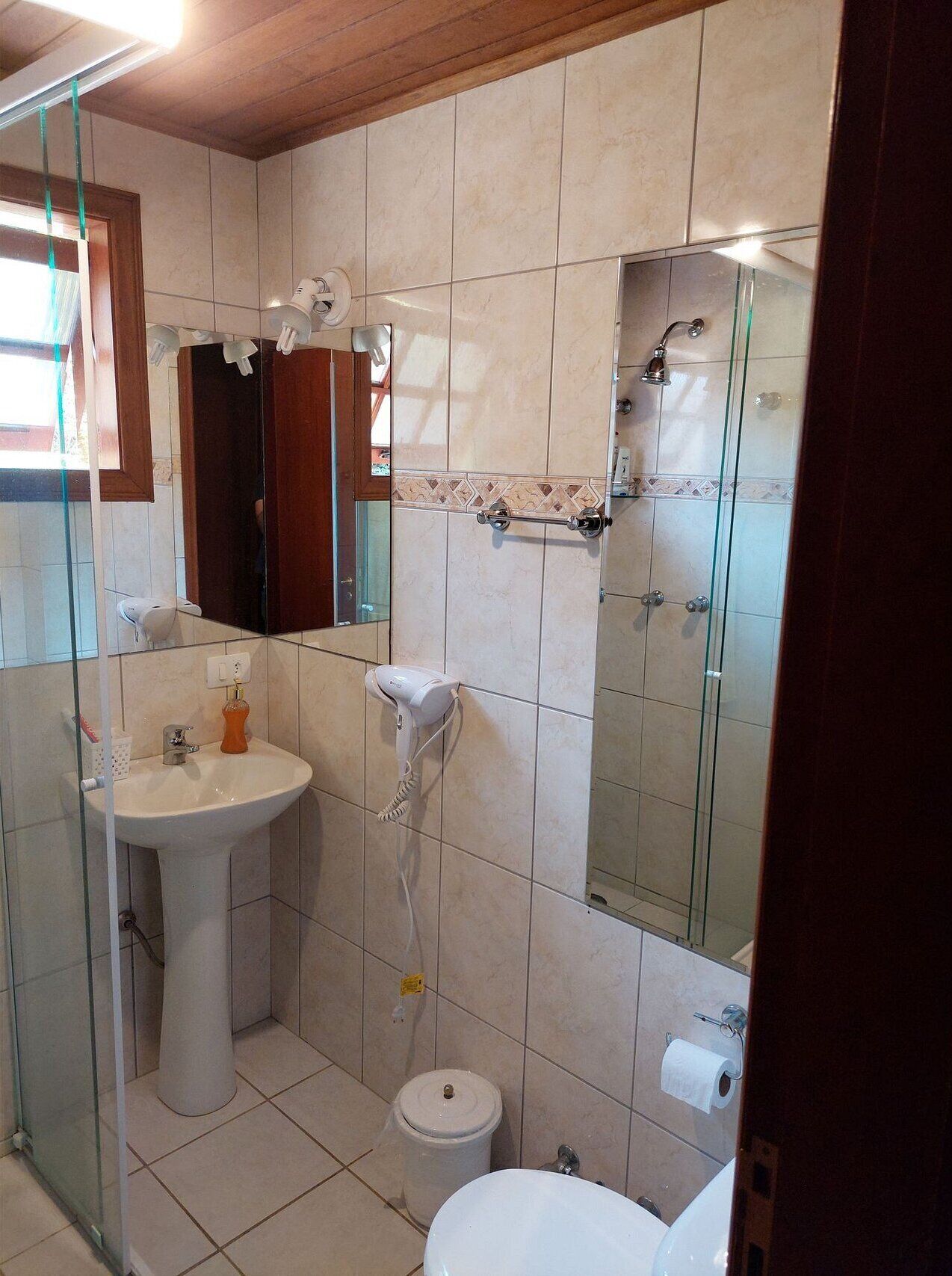 A bathroom with a pedestal sink, a handheld hair dryer, a toilet, and a shower area.