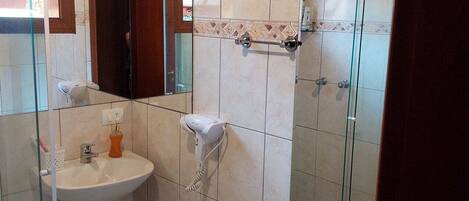 A bathroom with a pedestal sink, a handheld hair dryer, a toilet, and a shower area.