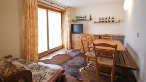 A room with a bed, a dining table with chairs, a television, and wine bottles on shelves.