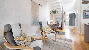 En moderne stue med to grå sofaer, mønstrede hynder og et macramé-ophæng, samt et køkken i baggrunden.