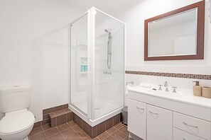 Ett modernt badrum med en duschavdelning med glasväggar, vita sanitetsartiklar och ett kaklat golv.