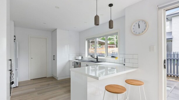 A modern kitchen with white cabinetry, a large island with bar stools, pendant lighting, and a window overlooking a backyard. - Contemporary with Courtyard by Sandy Bay Delights (Sandy Bay)