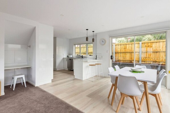 Una cocina moderna con armarios blancos, una isla central y una zona de comedor con mesa y sillas.