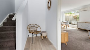 A modern interior with a staircase, a wicker chair, a small round table, and a view of a dining area through a glass door. - Contemporary with Courtyard by Sandy Bay Delights (Sandy Bay)
